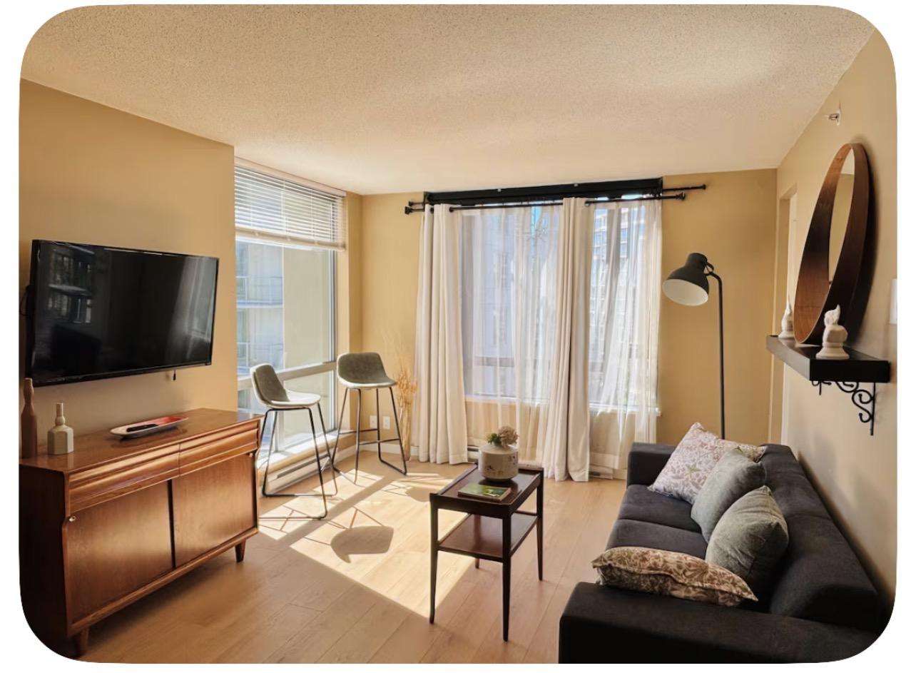 Sunlight filters through sheer curtains onto a gray sofa, wooden coffee table, and mid-century console. - property