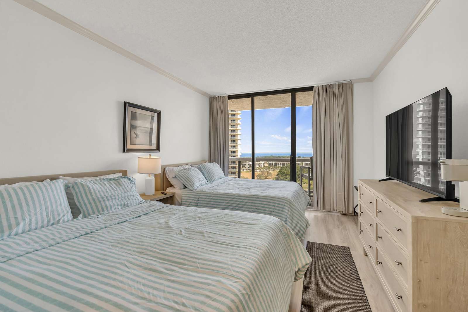 Bedroom features two queen beds, en-suite bathroom, and sliding glass door onto the private balcony with bay views. - property
