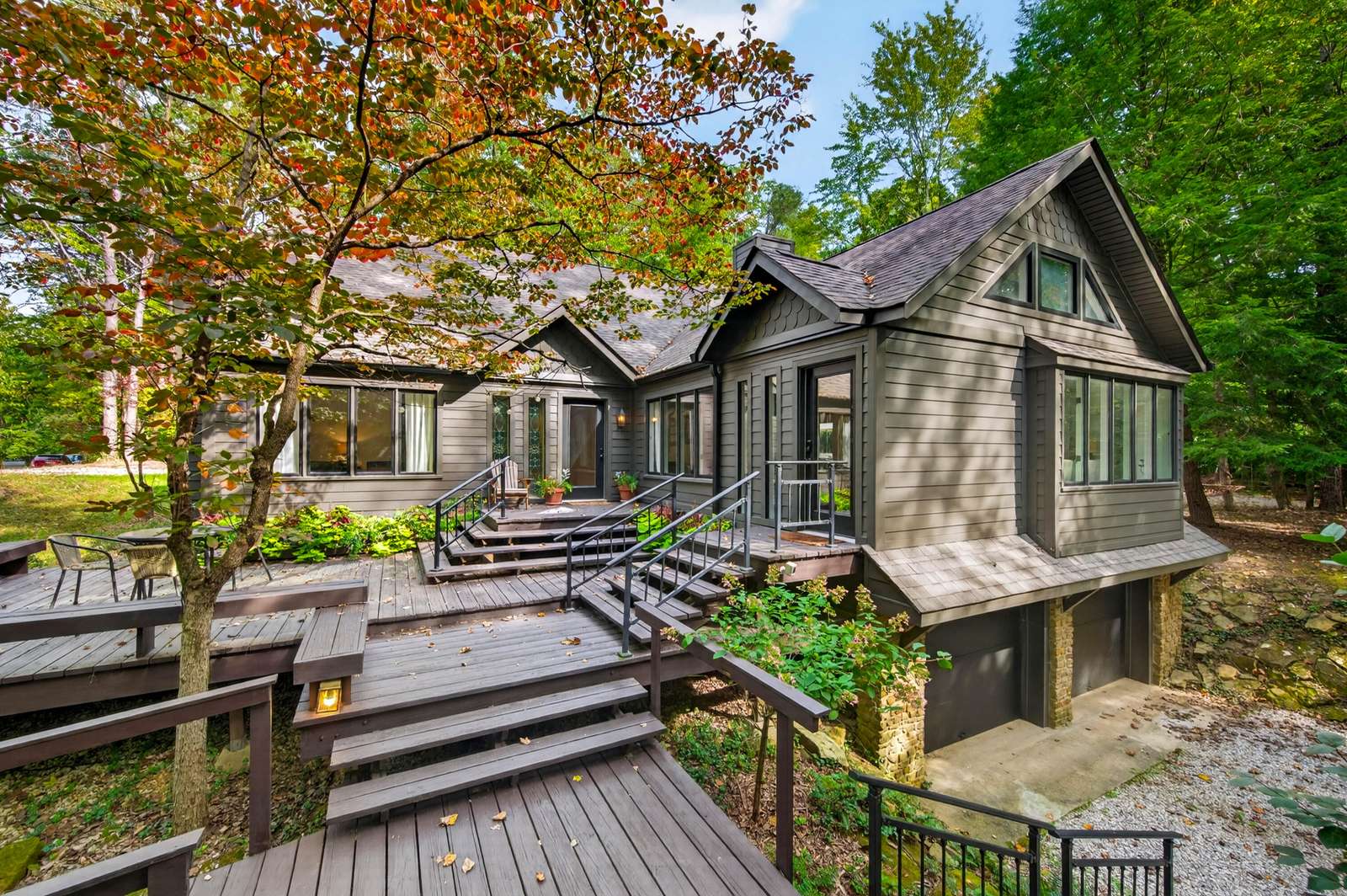 Multi-level wood deck with built-in benches and metal railings wraps around the gray siding exterior near a two-car garage. - property