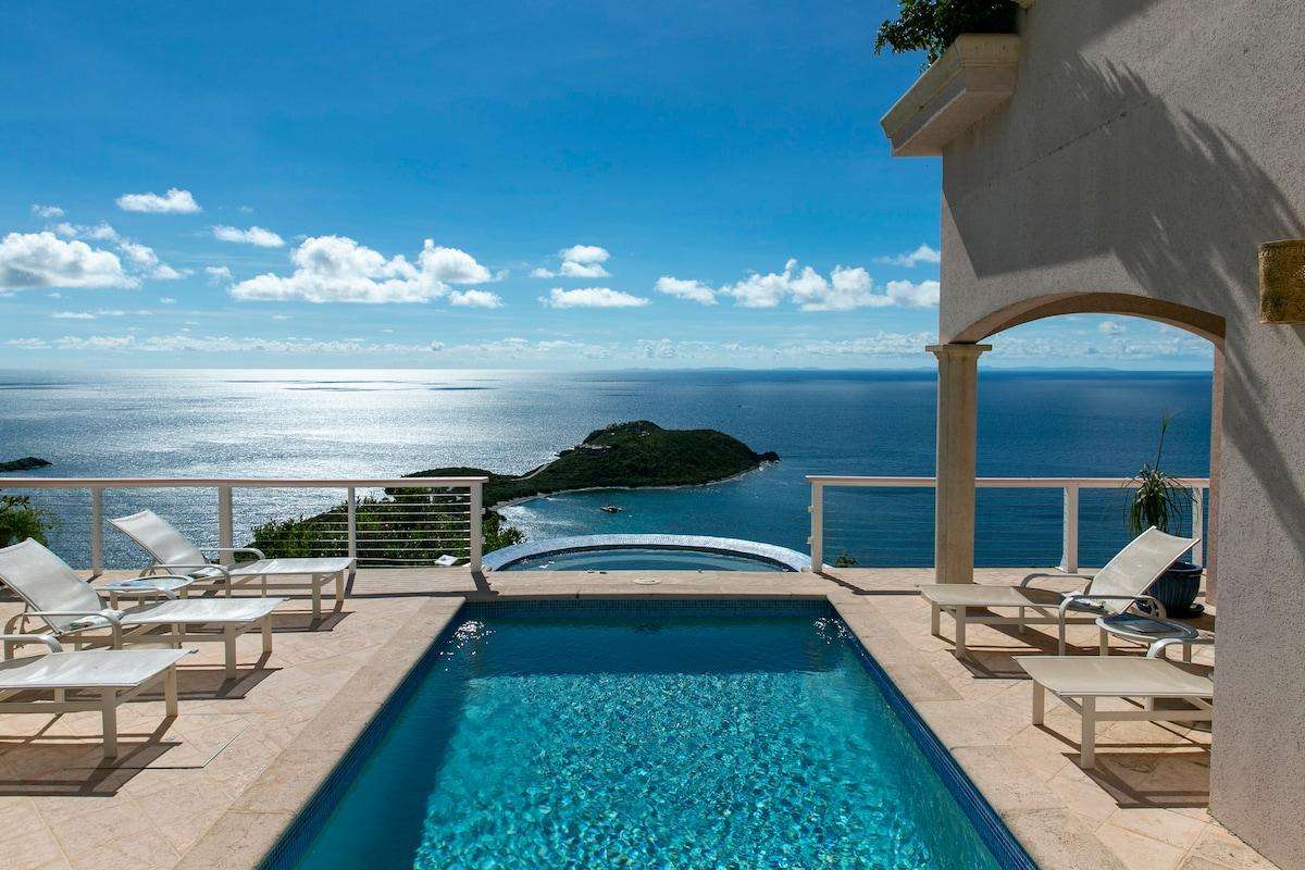 Sunlight sparkles on the blue pool surface, surrounded by cream stone tiles and white mesh loungers under a stucco arch. - property