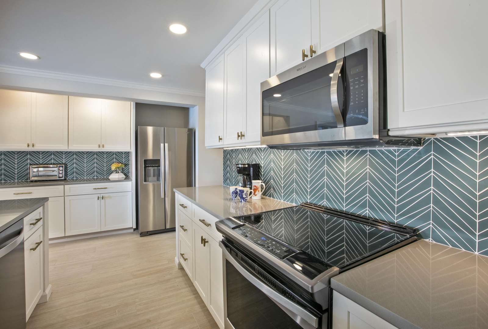 The kitchen features white cabinetry, brass hardware, and a gray chevron tile backsplash behind stainless steel appliances. - property