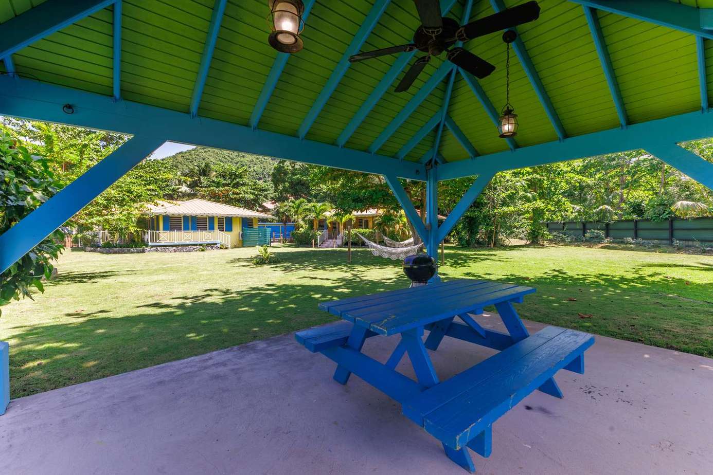 Shaded picnic pavilion with vibrant blue seating and lush lawn views