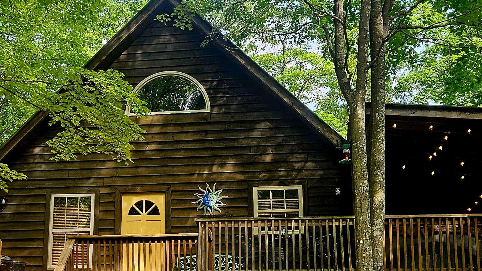 Dark wood-paneled cabin exterior with pale yellow door, sun-and-moon wall decor, and railing-surrounded porch. - property