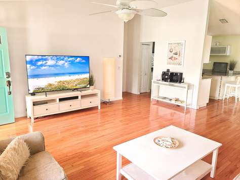 Open living area with honey-toned hardwood floors, white media console, and flat-screen TV against a pale wall.
