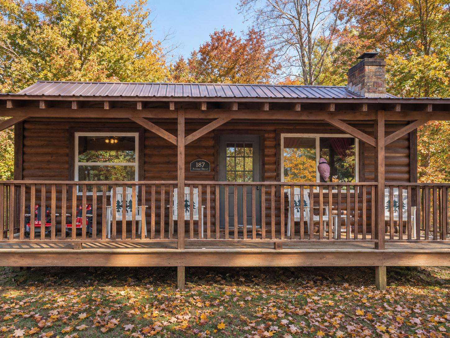 Front porch with wooden railings, log cabin exterior, rocking chairs, and autumn foliage surrounding the cabin. - property