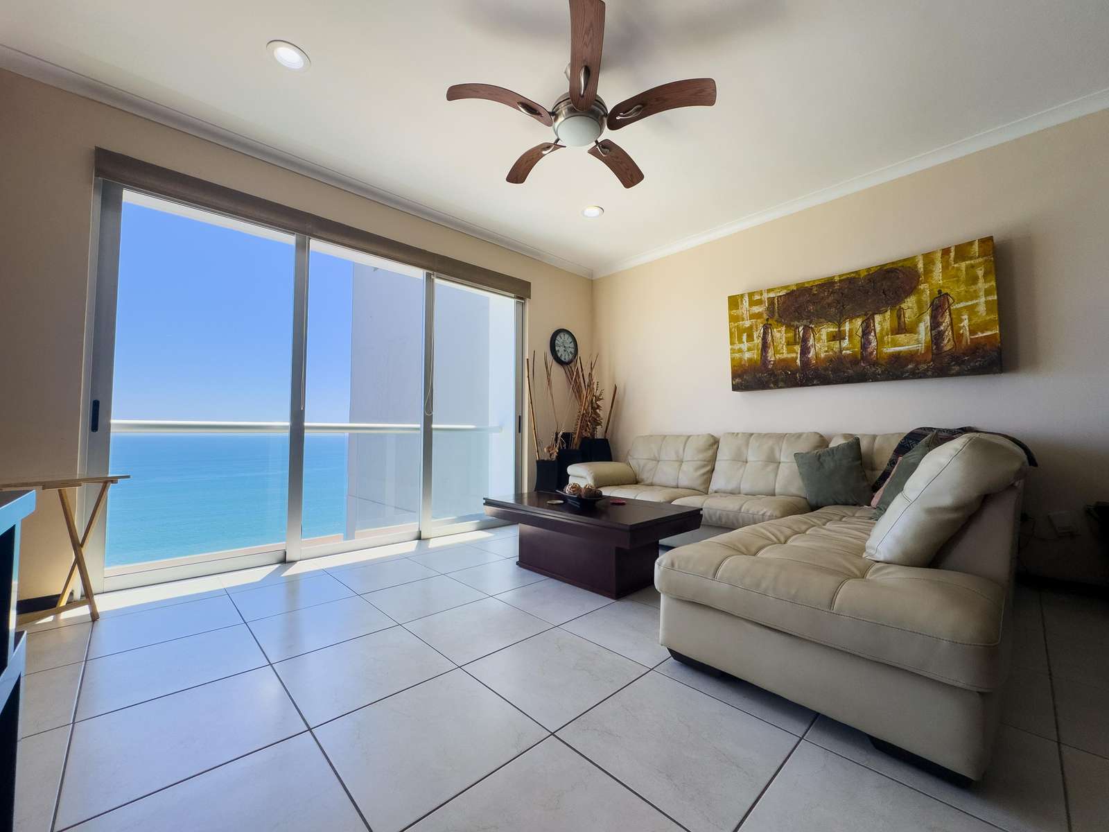 Sectional sofa in cream leather faces a dark wood coffee table, with sliding glass doors revealing ocean views. - property