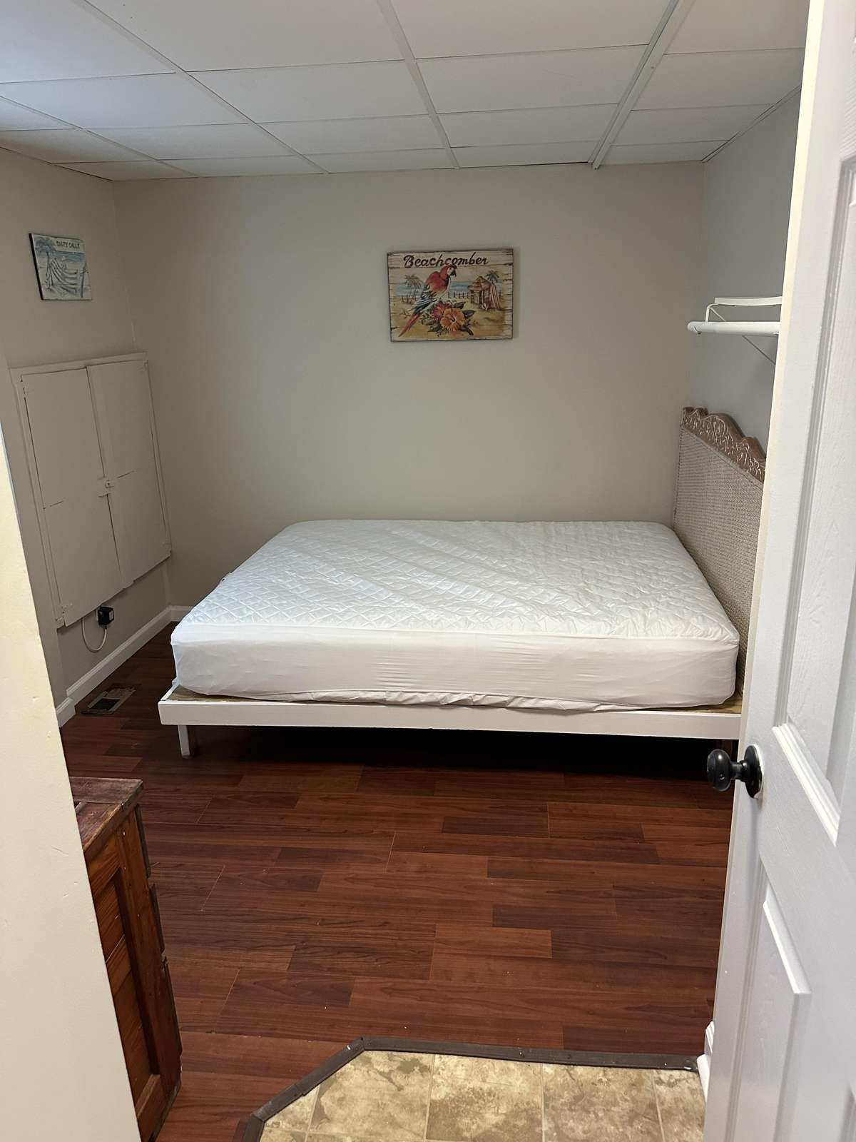 Bedroom with dark wood floors, white framed bed with quilted mattress, and coastal-themed wall art.