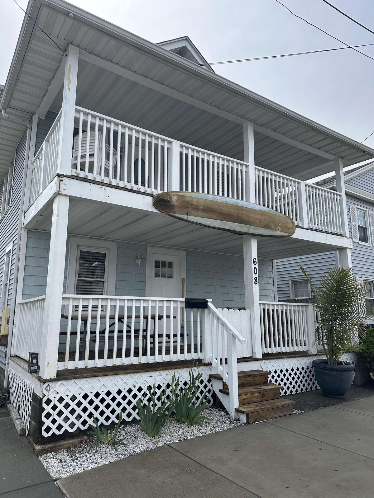 Two-story beach cottage with light blue siding, white railings, front porches, and a mounted wooden oar.