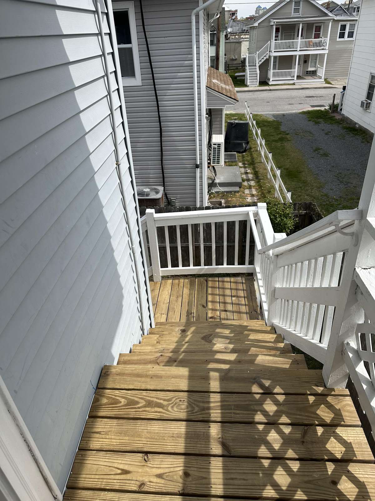 Exterior wooden staircase with white railing leads down from the second-floor porch, overlooking neighboring homes.