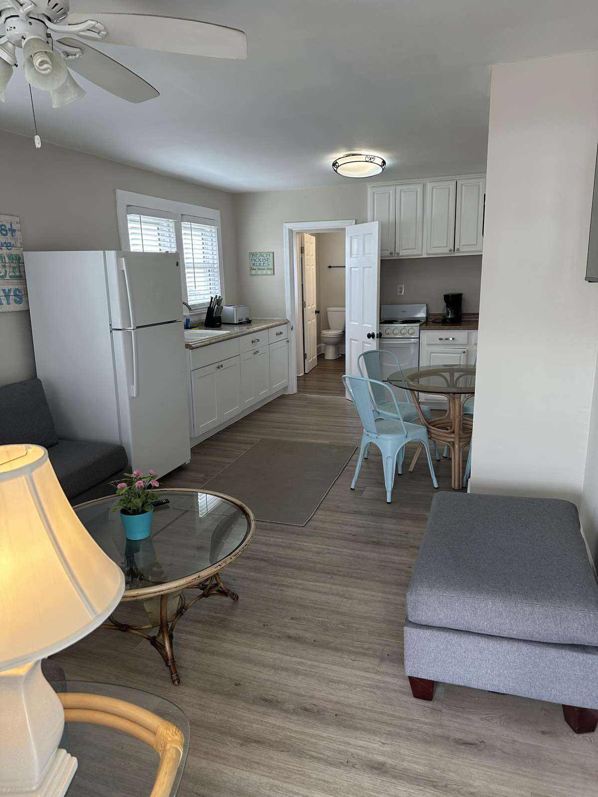Open-plan kitchen and dining area with white cabinets, glass-top table, and light gray wood-look flooring.
