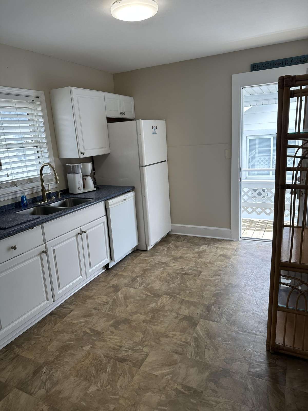 Kitchen area with white cabinetry, double sink, dishwasher, refrigerator, and tan vinyl tile flooring.