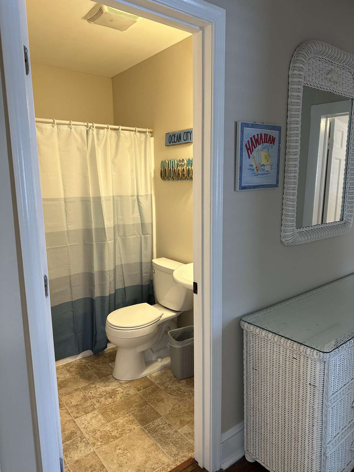 Bathroom with tan tile flooring, white toilet, striped blue-gray shower curtain, and coastal wall decor.