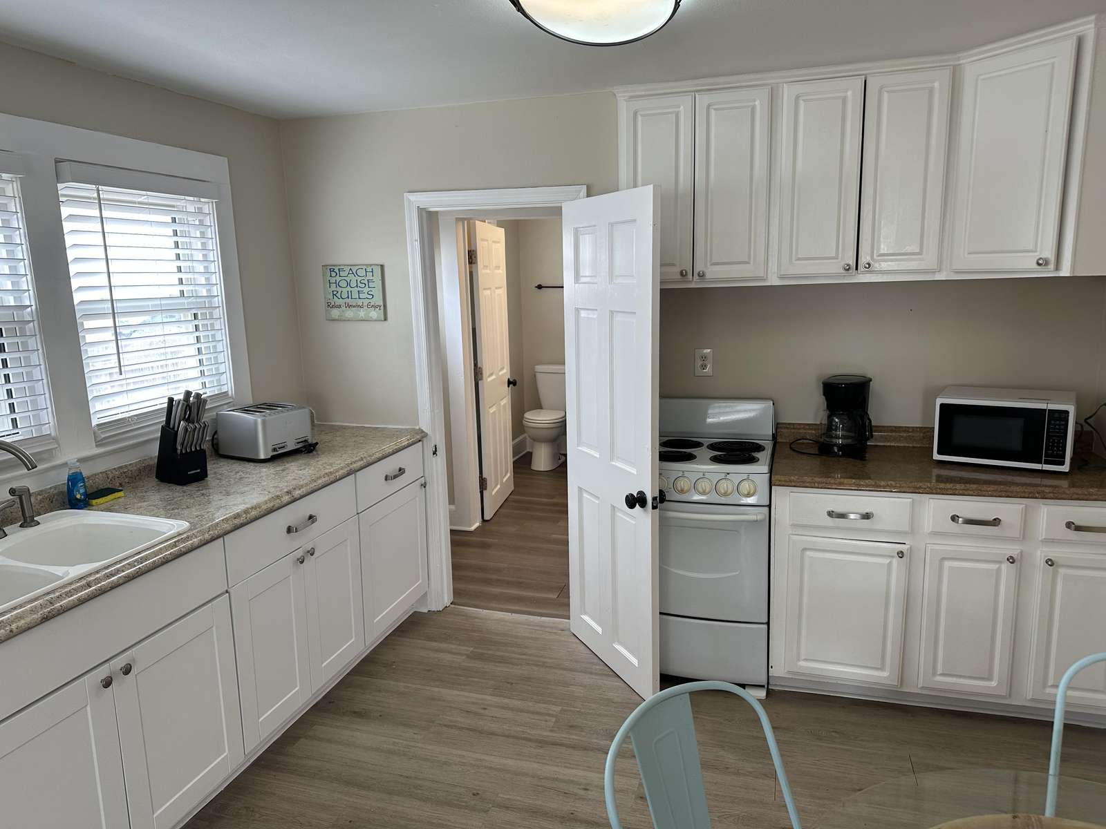 Kitchen with white cabinetry, granite-look countertops, electric stove, coffee maker, and microwave under soft natural light.