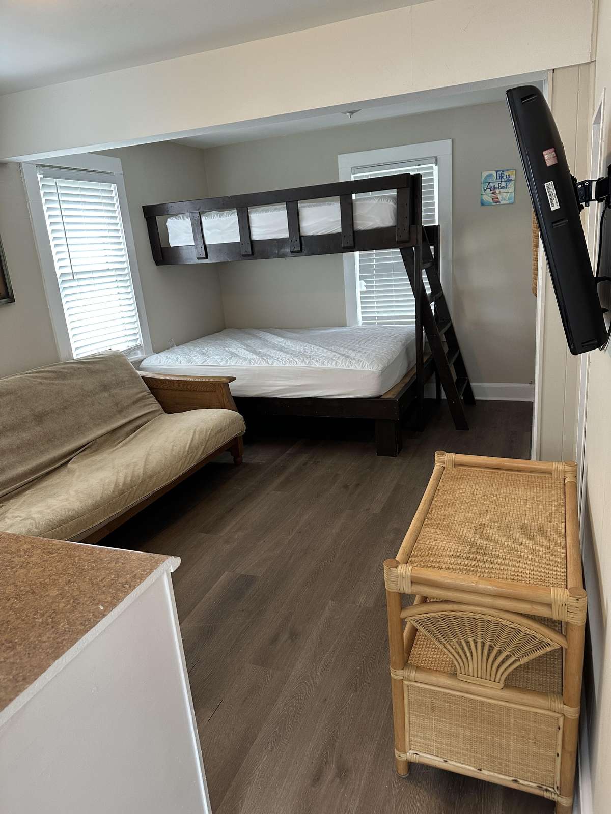 Sleeping area with dark wood bunk bed, beige futon, bamboo side table, and wall-mounted flat screen TV.