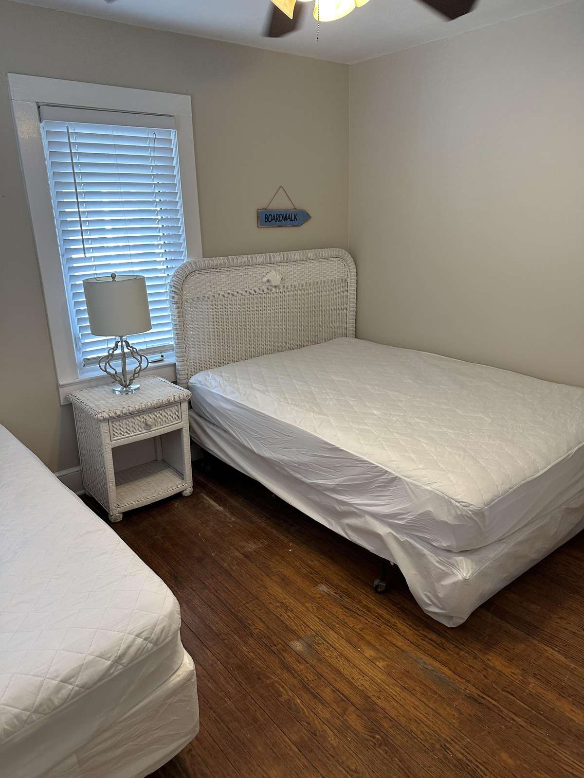 Two beds with white wicker headboards and a matching nightstand on dark hardwood flooring.