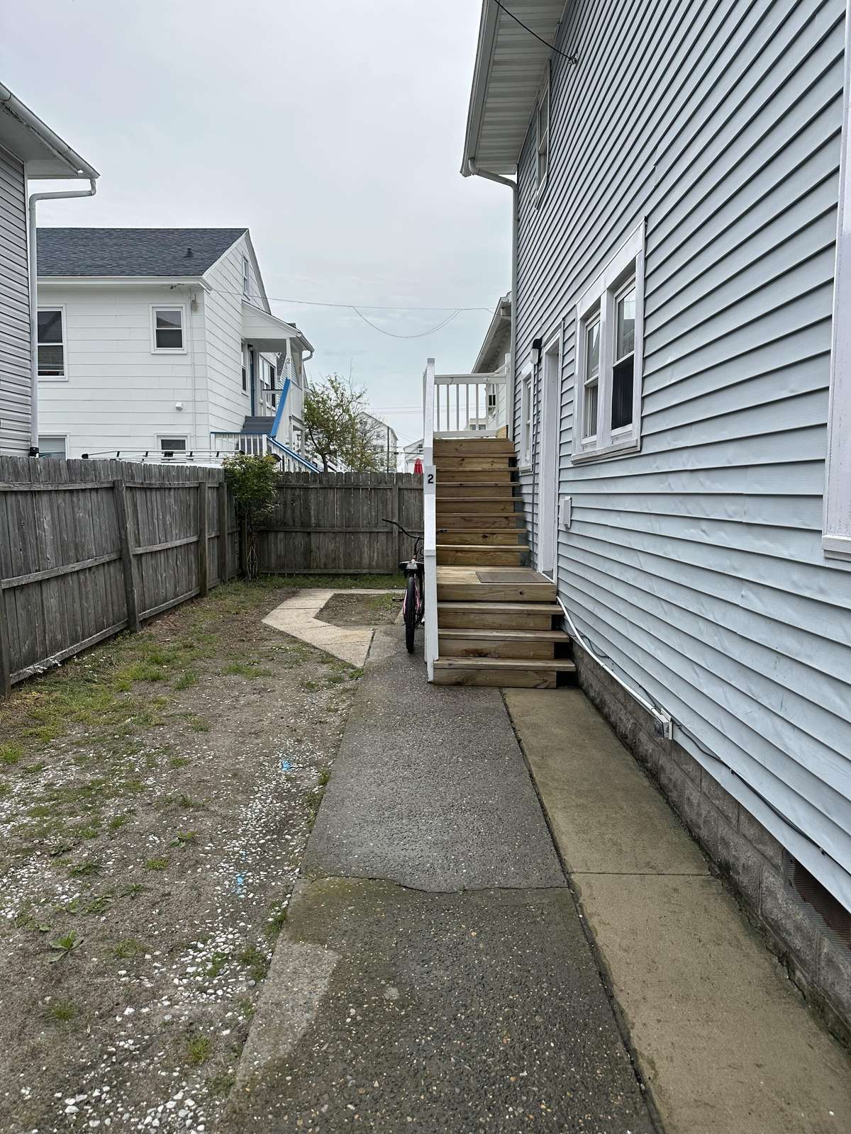 Side yard with wooden stairs leading to the second-floor entrance, bordered by a weathered wooden fence.