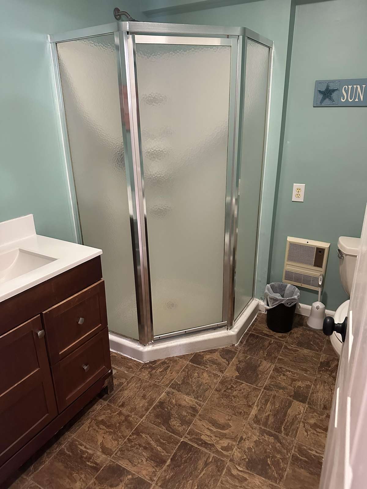 A corner shower with frosted glass and chrome frame stands next to a dark wood vanity and tiled floor.
