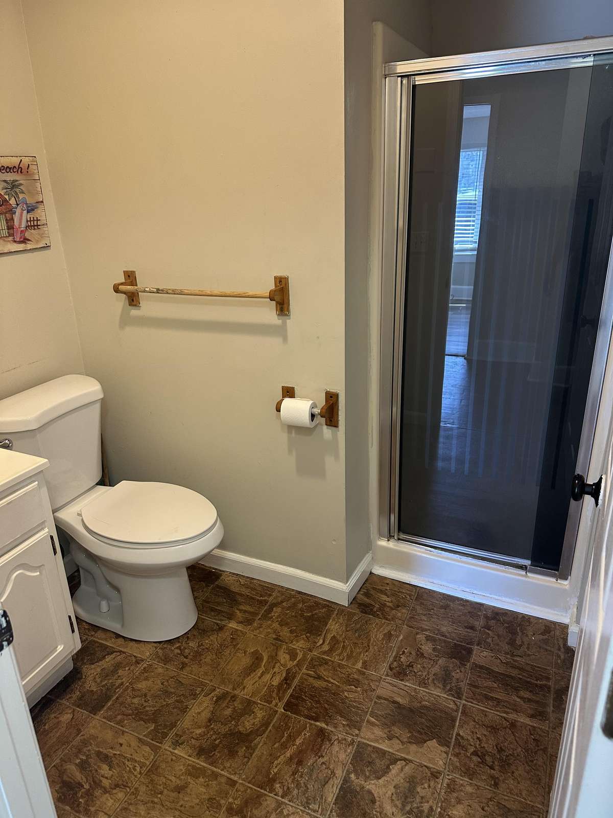 Bathroom with a white toilet, framed glass shower door, wood-tone tile floor, and light beige walls.