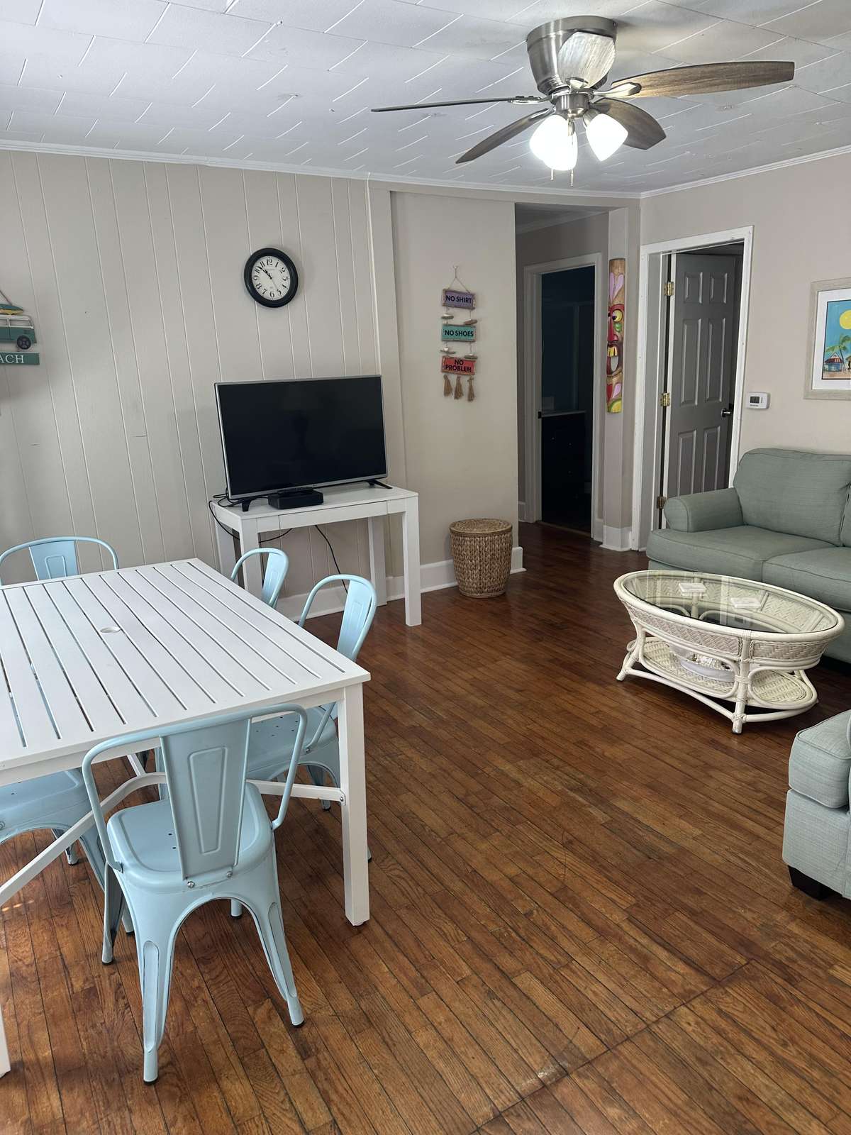 Wood floors ground the living area with a rattan coffee table, sage sofas, and a wall-mounted flat-screen TV.