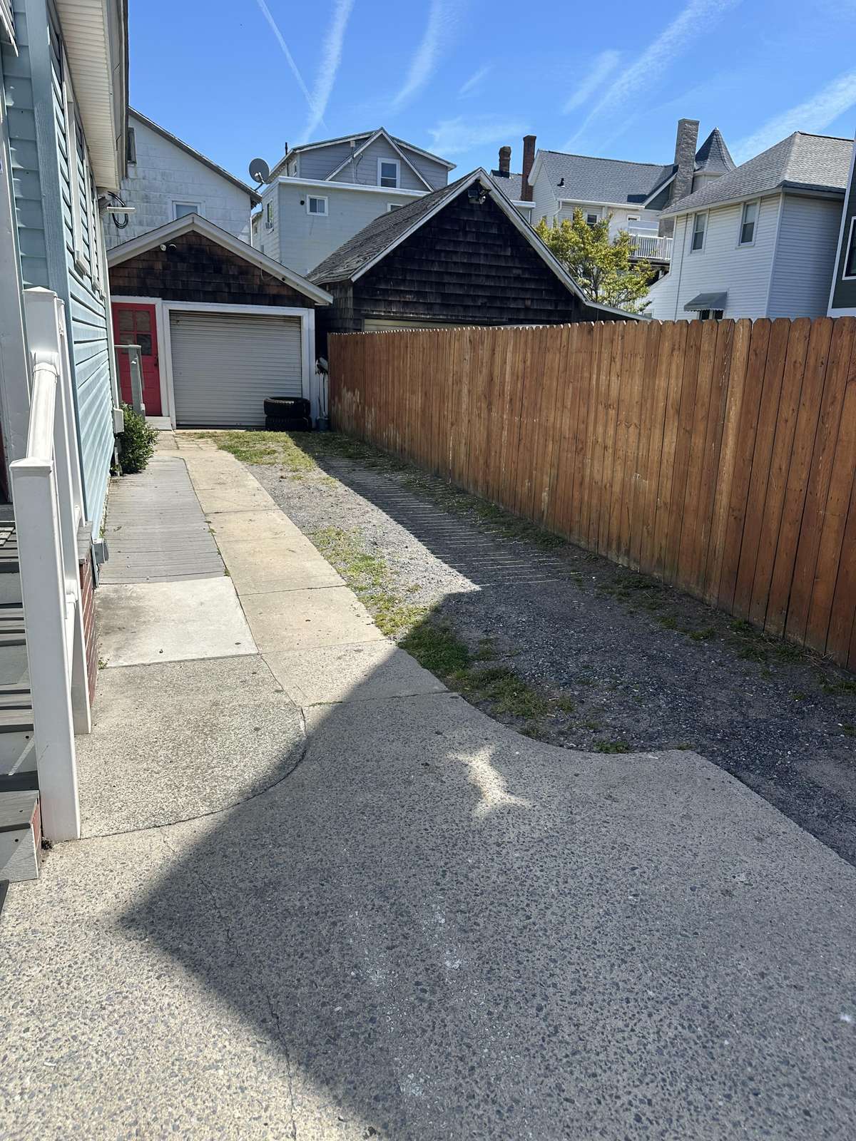 Gravel driveway runs alongside the blue-sided house, leading to a detached garage with a red door.