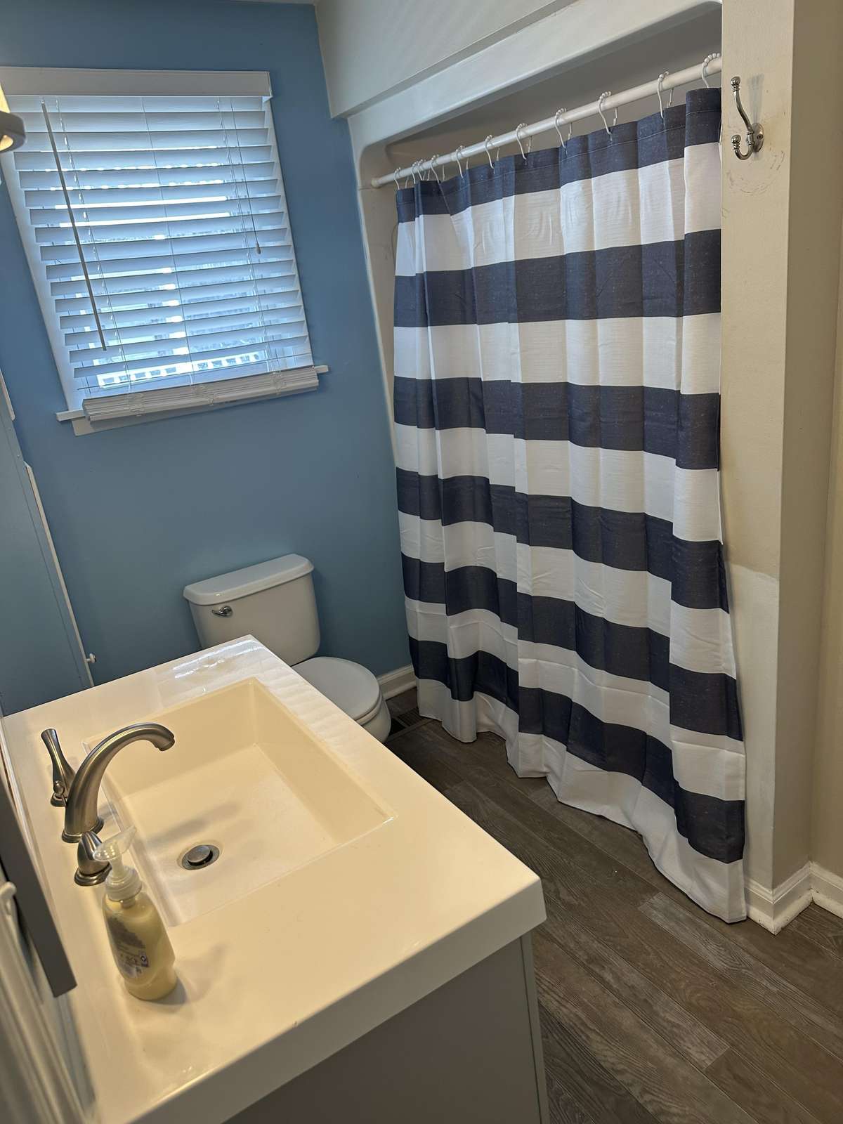 Bathroom features a white vanity sink, striped navy and white shower curtain, and wood-look flooring.