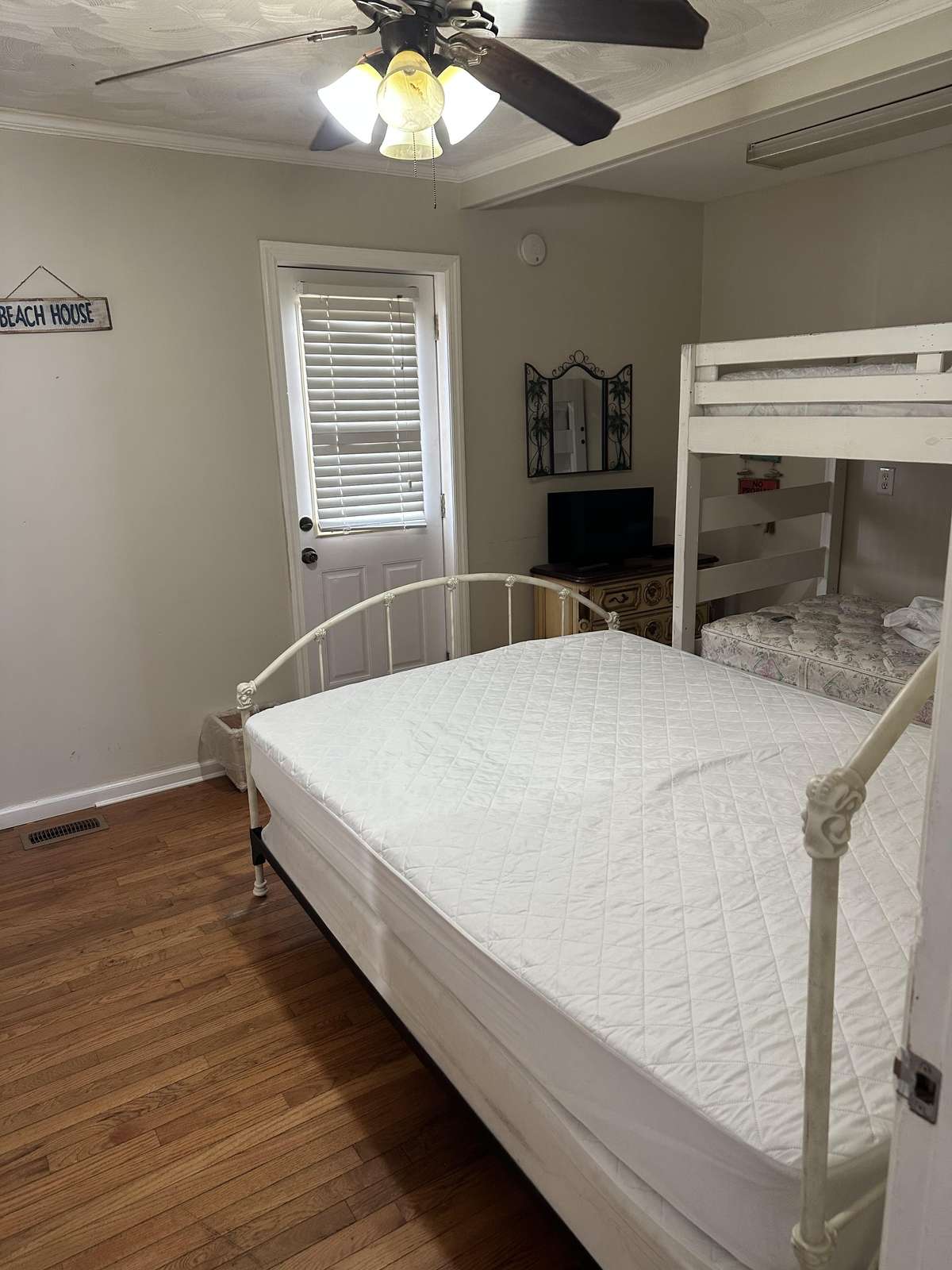 Bedroom with white metal bed frame, bunk beds, hardwood floors, ceiling fan, and a small TV on vintage dresser.