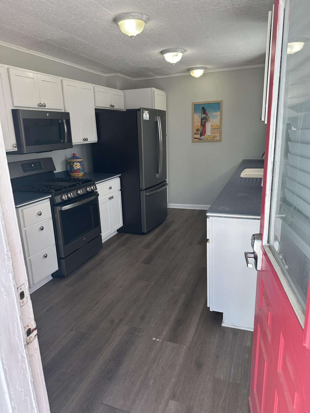 Red exterior door opens to a galley kitchen with white cabinetry, dark countertops, and stainless steel appliances.