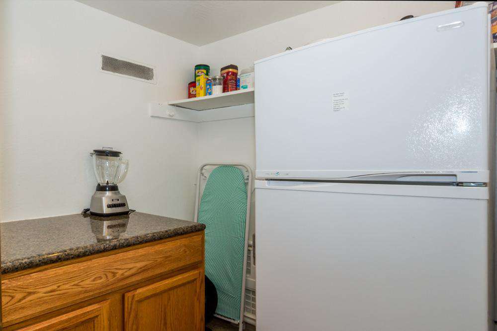 Walk-in closet behind kitchen w/refrigerator and ironing board.