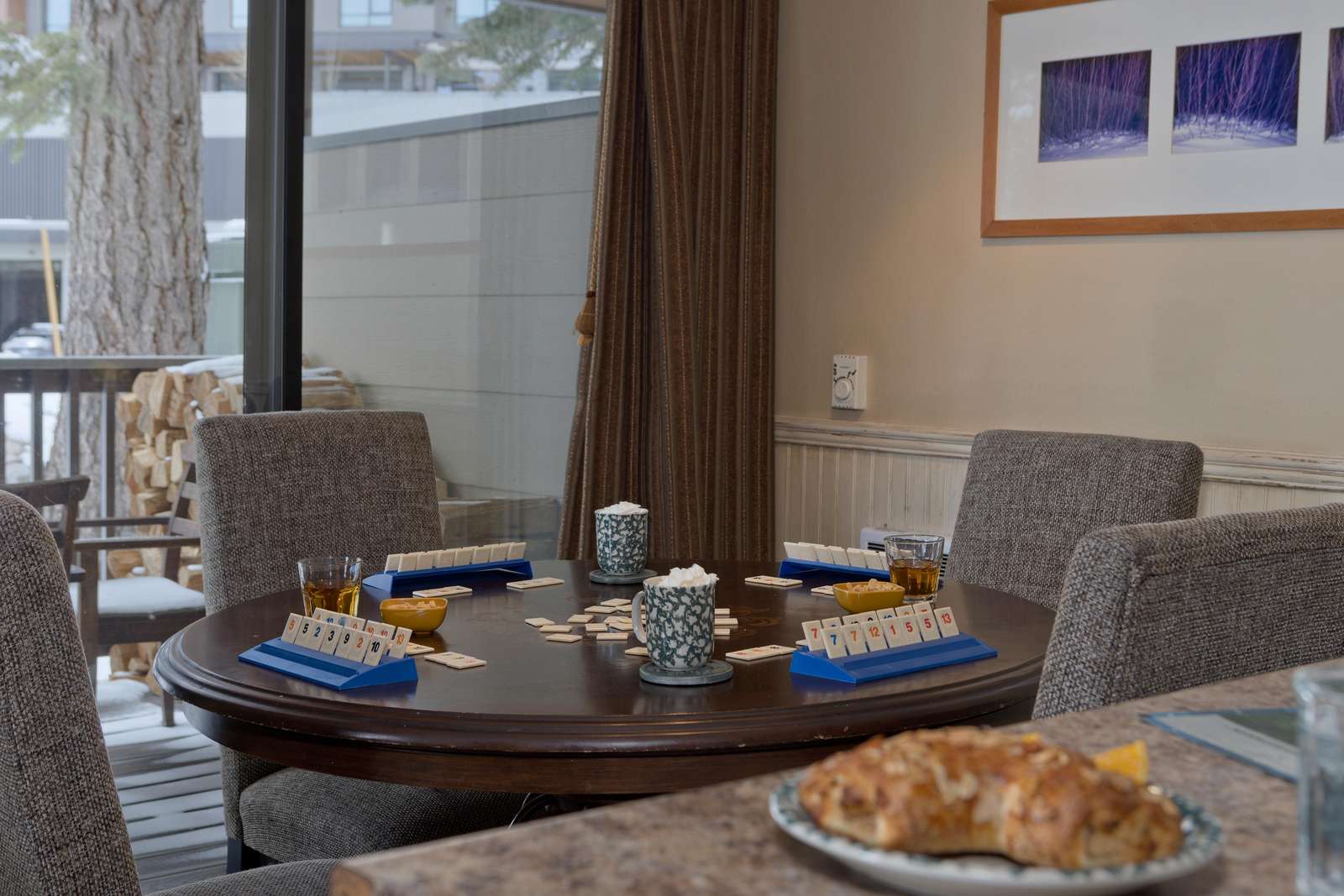 Round dining table set for a game with blue racks, patterned mugs, and plush gray chairs near sliding glass doors. - property