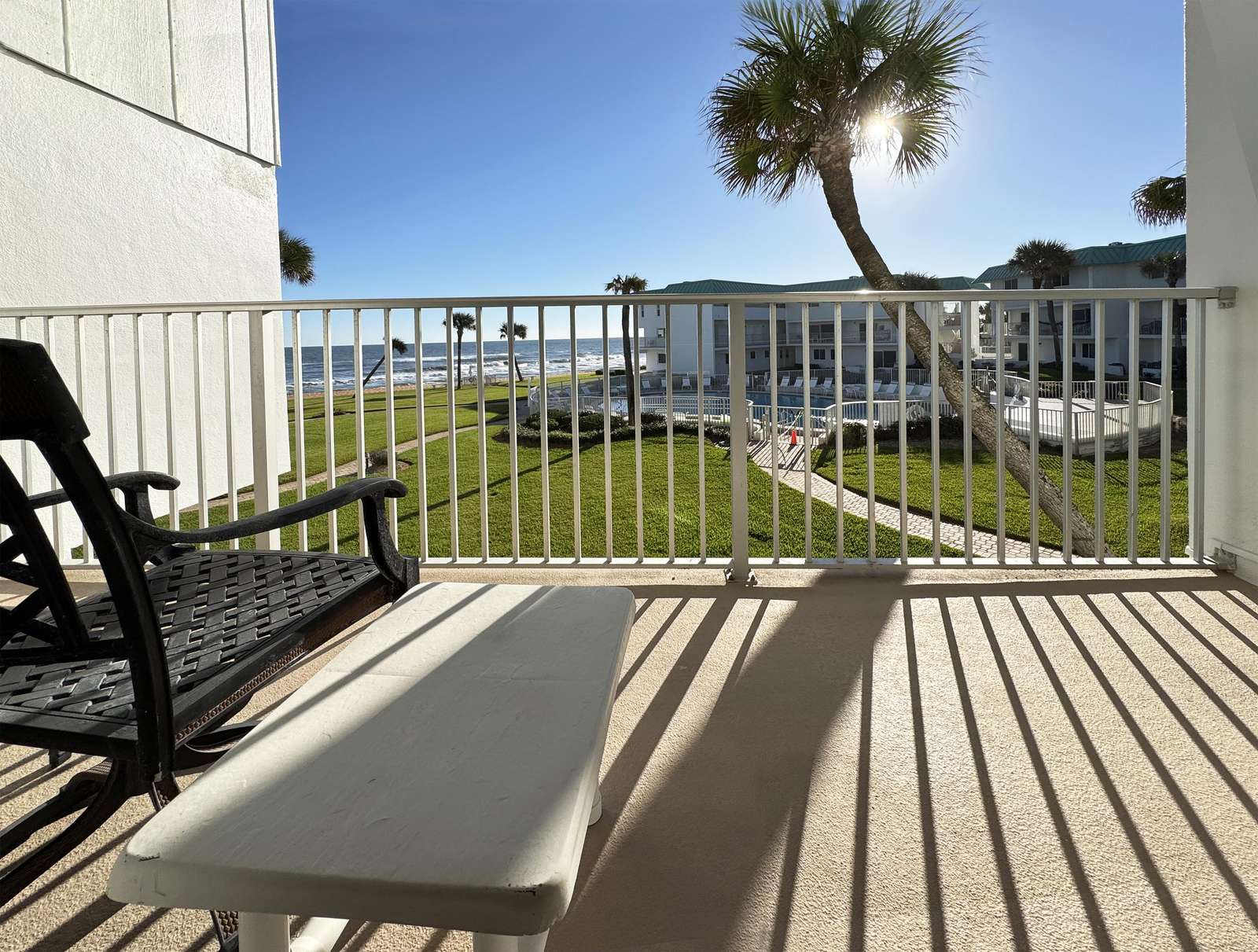 Sunlit balcony with serene water and palm tree views - property