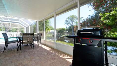 Screened patio with brick pavers, black metal dining set, gas grill, and lake views beyond the enclosure.