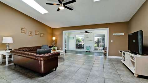 Living room features a brown leather tufted sofa, white side tables, and a skylight above tiled floors.