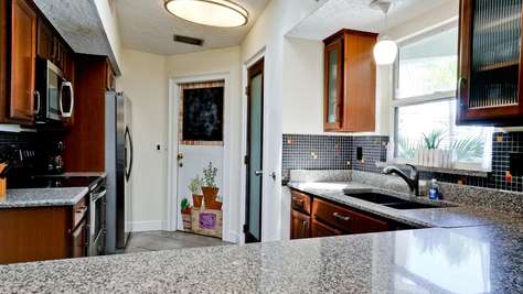 Granite countertops complement dark wood cabinets and black mosaic tile backsplash in the kitchen.