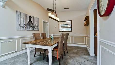 Rectangular wooden dining table with white legs and six wicker chairs on gray tile floor.