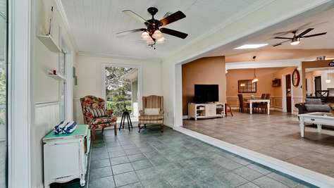 Sunroom with green tiled floor, floral and striped armchairs, white walls, and ceiling fan lighting.