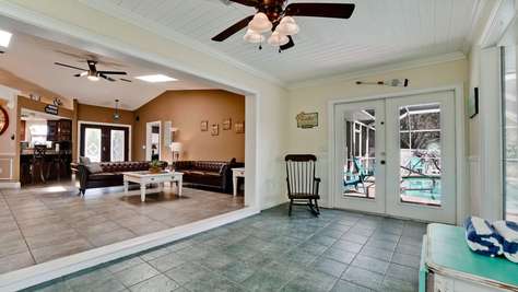 Entryway features green stone tile floor, white trim, ceiling fan, wooden rocking chair, and glass doors to pool deck.