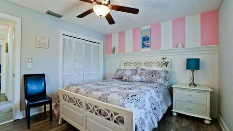A white wood bed with patterned bedding is set against pink and white striped walls in the bedroom.