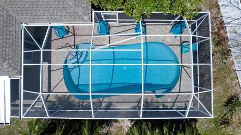 Heated kidney-shaped pool with curved steps, surrounded by a screened enclosure and six blue Adirondack chairs.