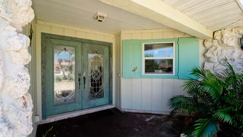 Front entry with double glass-paneled doors, seafoam green shutters, and textured coral stone accents.