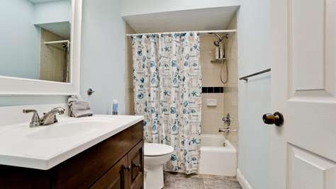 Bathroom with sea-themed shower curtain, beige tiled tub surround, dark wood vanity, and light blue walls.