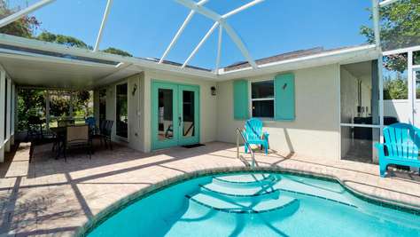 Heated pool with curved steps sits beside a turquoise French door and matching shutters on a brick patio.