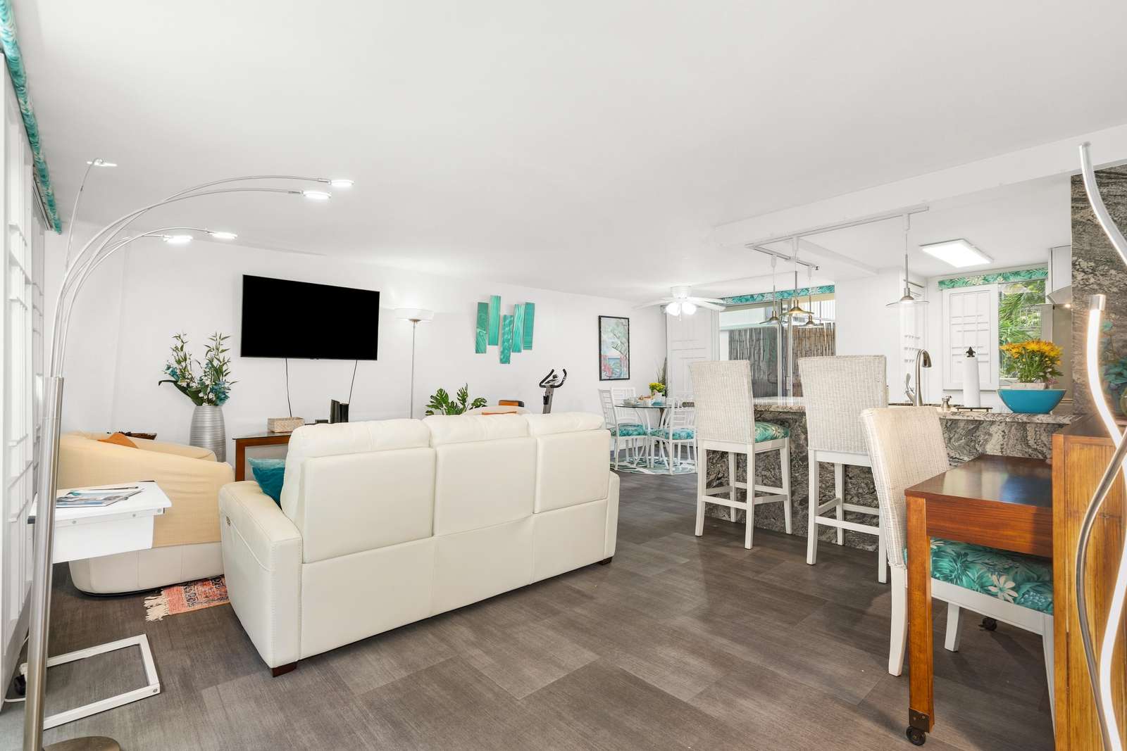 Dark wood floors extend through the open living, dining, and kitchen areas illuminated by arched floor lamps and ceiling fans.