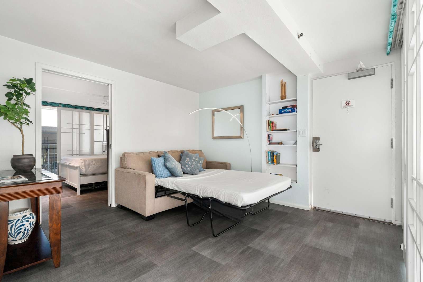 Pull-out sofa bed with patterned blue pillows sits against a pale blue accent wall beside built-in white shelves.