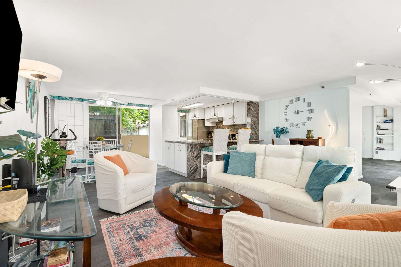 White leather sofa and armchairs frame a round wood and glass coffee table on a patterned rug in the living room.