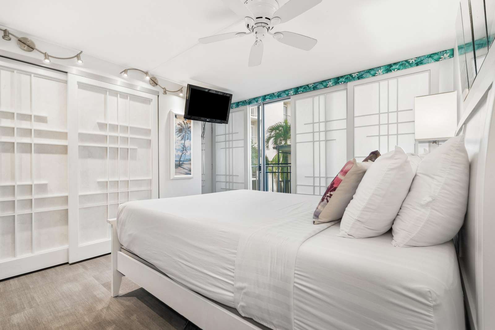 Bedroom features a white platform bed with layered pillows, sliding shoji-style closet doors, and a wall-mounted TV.