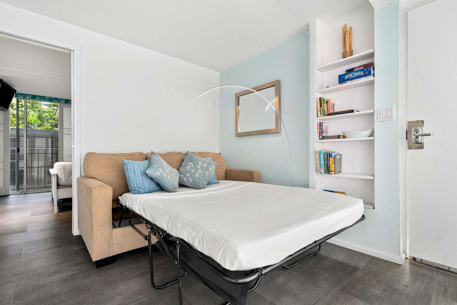 Living room features a beige sofa bed with blue patterned pillows, an arched floor lamp, and built-in white shelves.