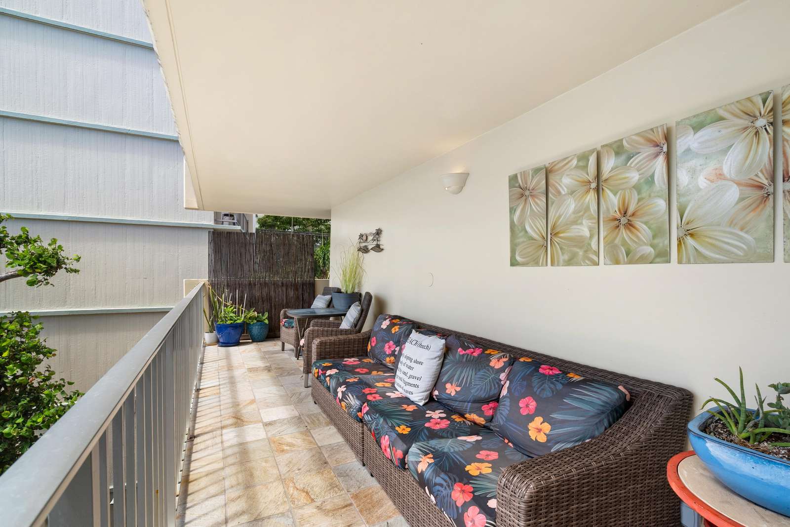 Wicker sofa with floral cushions and matching chairs line the tiled balcony with tropical artwork above.