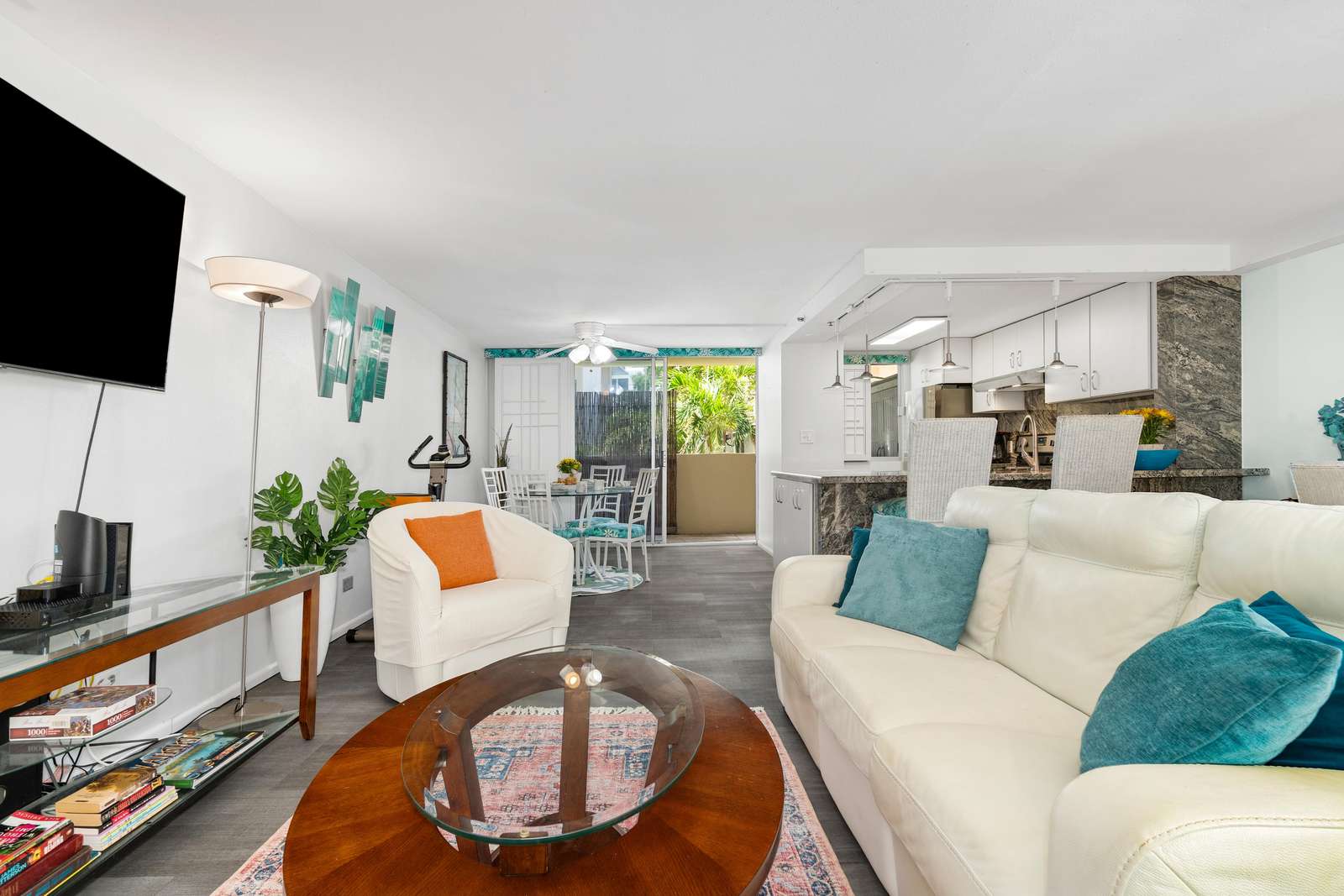 Cream leather sofa with teal pillows faces a round wood and glass coffee table on a patterned rug in the living area.