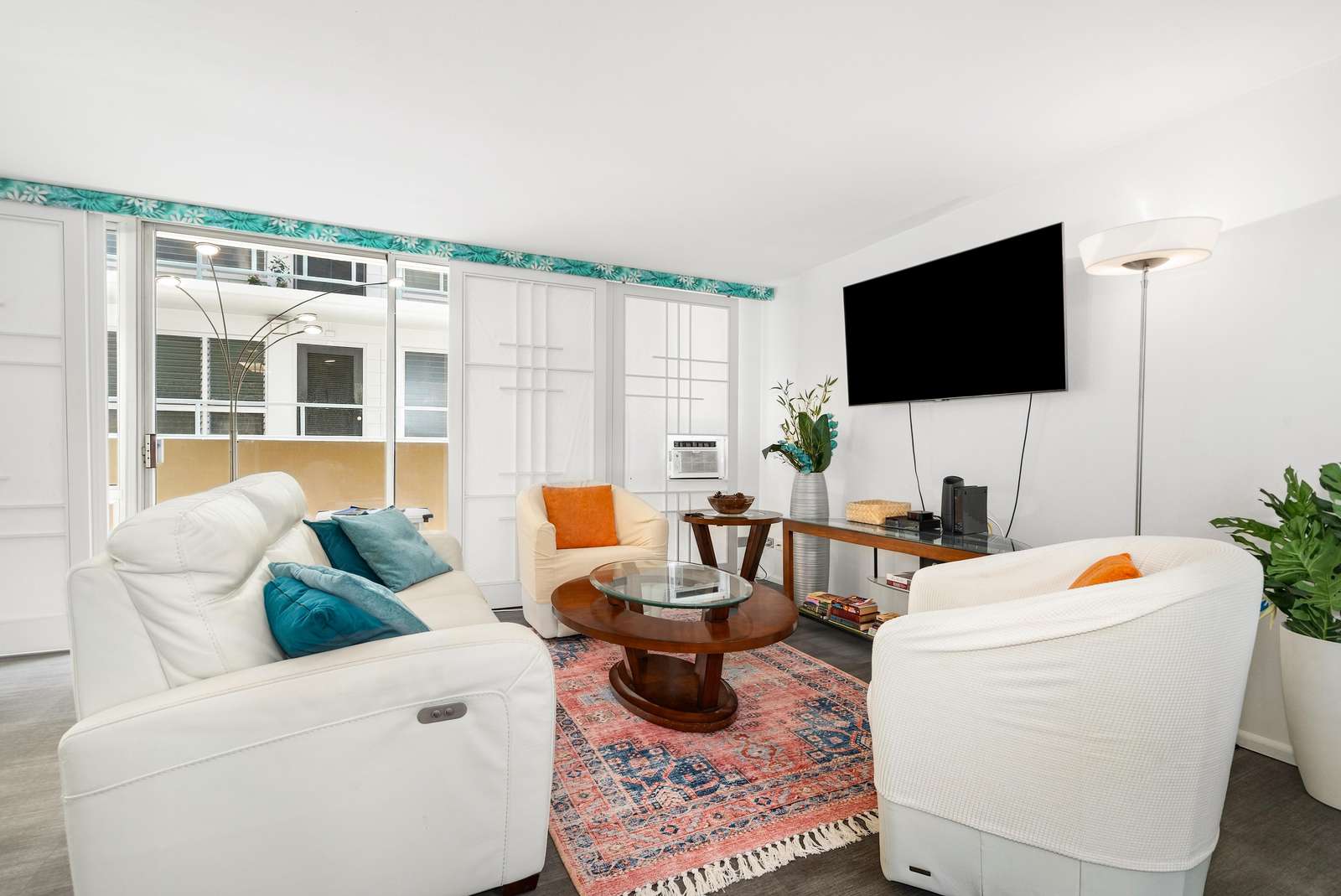 A patterned rug anchors the seating area with white swivel chairs, a reclining sofa, and a wood and glass table.