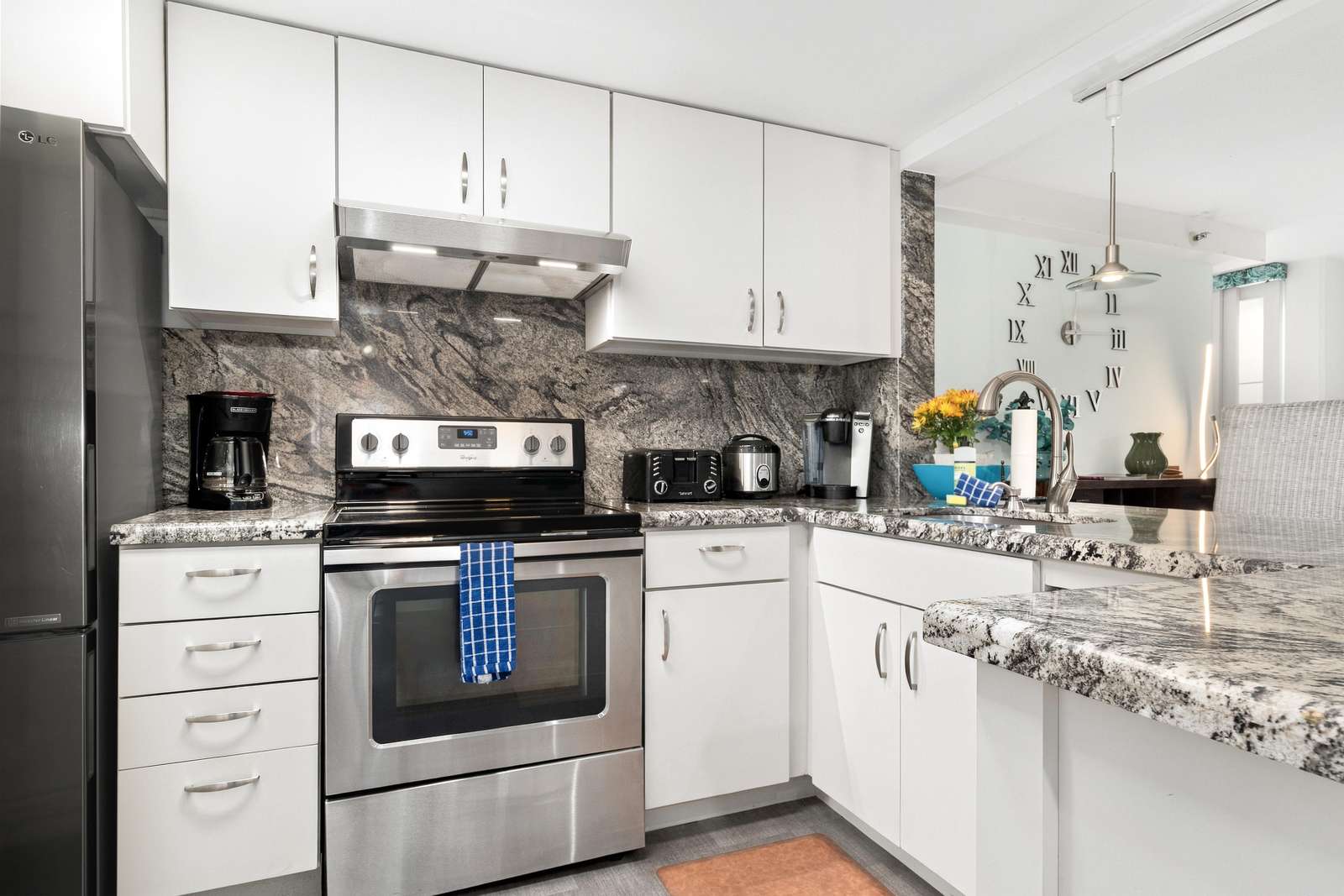 Granite countertops and backsplash complement white cabinetry and stainless steel appliances in the kitchen.